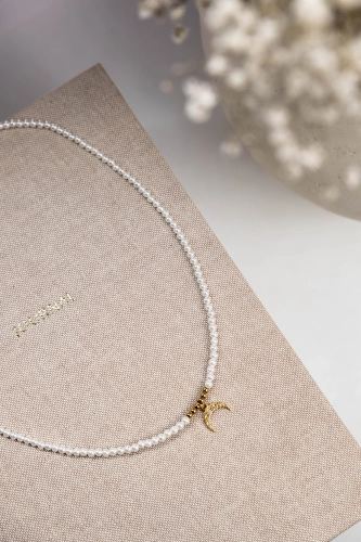 Helle Crystal Moon Halskette aus Seashell-Perlen mit goldfarbenem Lunula-Anhänger auf beigem Stoff