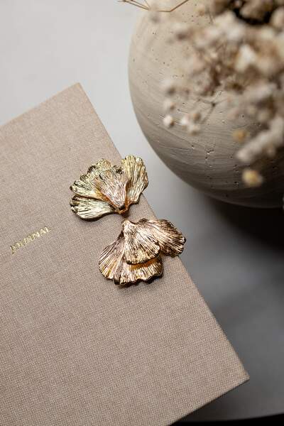 Goldene Golden-Flowers-Petals-Ohrringe in Blütenform auf einer beigen Schmuckbox
